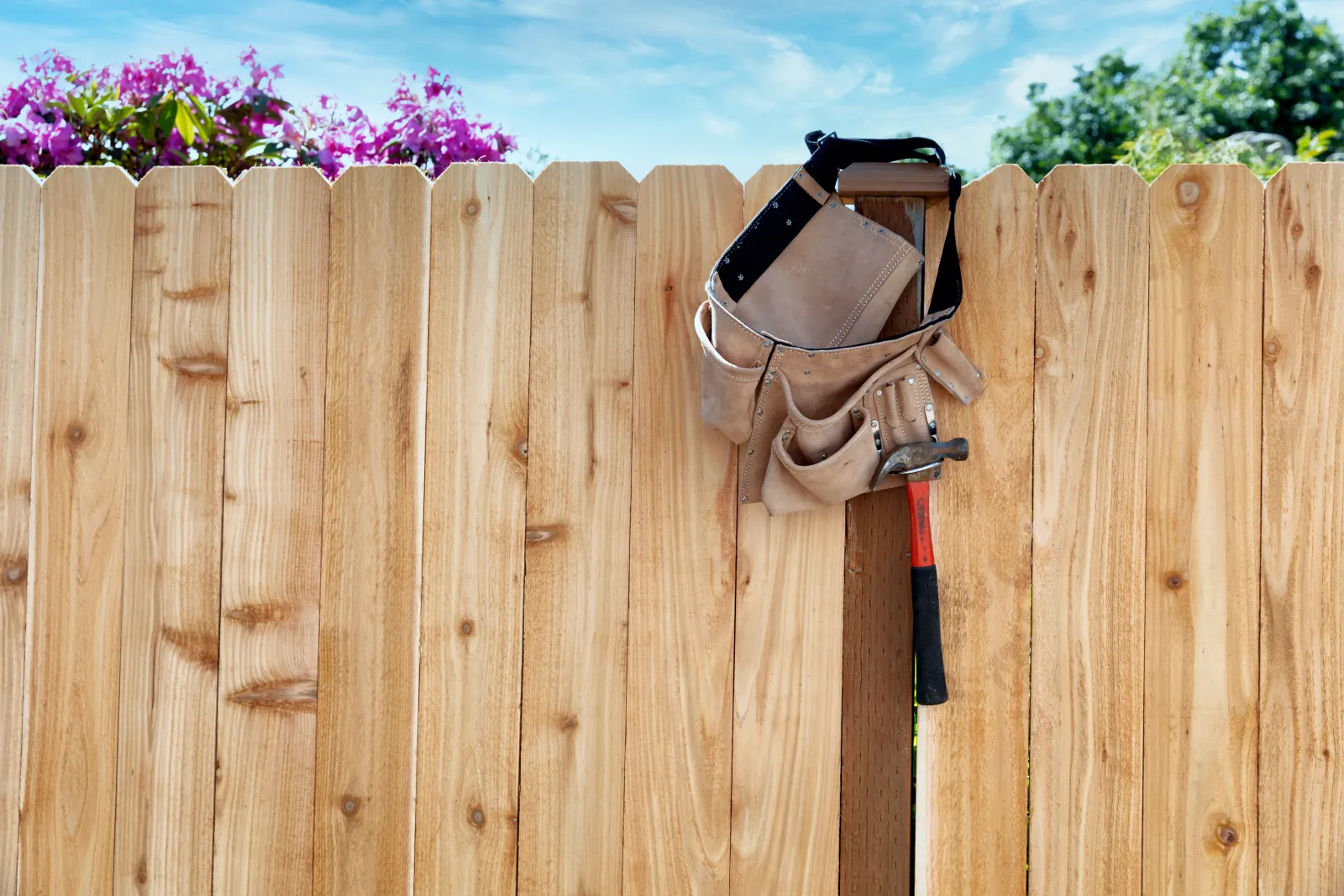 Newly installed cedar wood fence with a contractor's tool belt and hammer — residential fence installation in Austin.