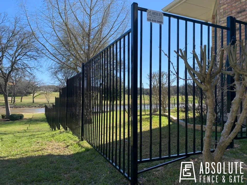 Black ornamental steel fence along the side of a brick home